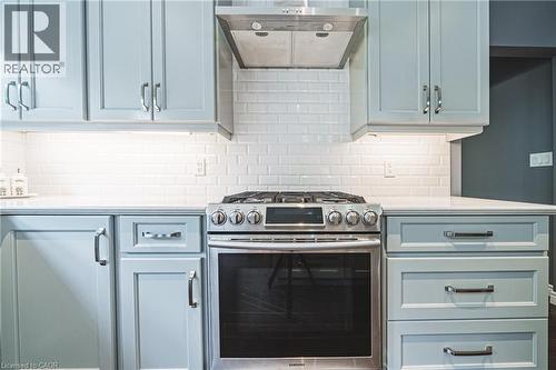 Kitchen featuring stainless steel range with gas stovetop, exhaust hood, light stone counters, decorative backsplash, and blue cabinets - 25 Orchard Hill, Hamilton, ON - Indoor Photo Showing Kitchen