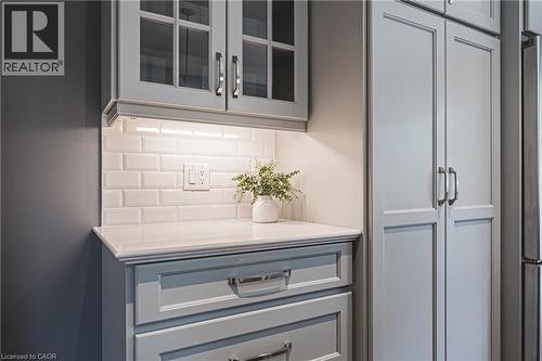 Kitchen view of backsplash, glass insert cabinets, gray cabinetry, light stone countertops, and freestanding refrigerator - 25 Orchard Hill, Hamilton, ON - Indoor