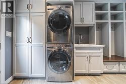 Laundry area with estacked washer and dryer, cabinet space, and light wood finished floors - 