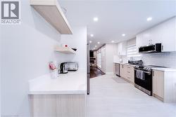 Kitchen featuring white cabinetry, light stone countertops, tasteful backsplash, light tile patterned floors, and appliances with stainless steel finishes - 