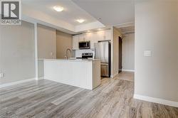 Kitchen featuring appliances with stainless steel finishes, light countertops, light wood finished floors, a peninsula, and a tray ceiling - 
