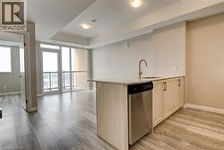 Kitchen featuring light brown cabinets, expansive windows, stainless steel dishwasher, a peninsula, and light wood-style flooring - 