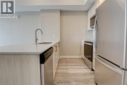 Kitchen with stainless steel appliances, a peninsula, light wood-style flooring, light stone countertops, and white cabinetry - 