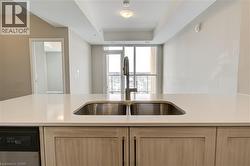 Kitchen with light brown cabinets, dishwasher, a raised ceiling, and light stone countertops - 