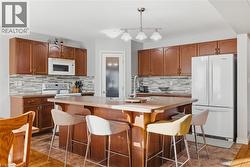 Kitchen with pendant lighting, white appliances, brown cabinetry, light countertops, and a center island with sink - 