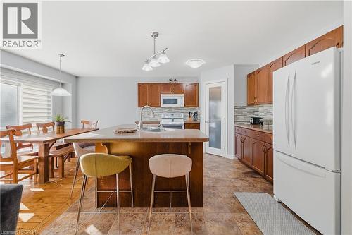 Kitchen with white appliances, decorative light fixtures, a kitchen bar, and light countertops - 23 Doon Creek Street, Kitchener, ON - Indoor