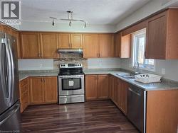 Kitchen with stainless steel appliances, wood finish cabinetry, dark wood finished floors, a textured ceiling, and light countertops - 