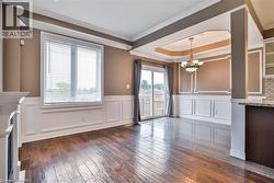 Unfurnished dining area featuring dark wood-style flooring, crown molding, a wainscoted wall, suspended lighting, and a tray ceiling - 