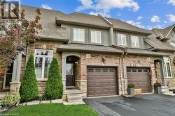 View of front of property featuring a shingled roof, an attached garage, driveway, and stone siding - 