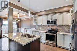 Kitchen with glass fronted cabinets, stainless steel appliances, a center island with sink, light stone counters, and ornamental molding - 