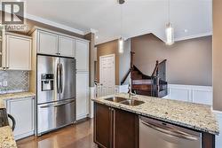 Kitchen featuring stainless steel appliances, pendant lighting, light stone counters, ornamental molding, and backsplash - 