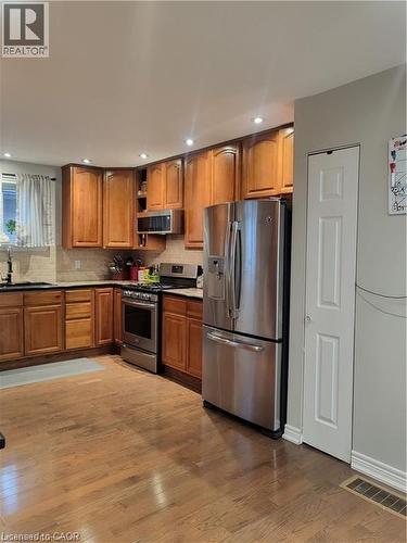 Kitchen with appliances with stainless steel finishes, brown cabinetry, wood finished floors, open shelves, and recessed lighting - 18 Rosewell Street, Hamilton, ON - Indoor Photo Showing Kitchen With Stainless Steel Kitchen