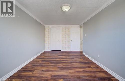 Unfurnished bedroom with dark wood-style floors, a textured ceiling, crown molding, a closet, and wallpapered walls - 54 Nicklaus Drive, Hamilton, ON - Indoor Photo Showing Other Room