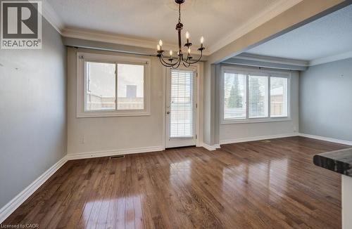 Unfurnished dining area with dark wood-type flooring, ornamental molding, a chandelier, a textured ceiling, and plenty of natural light - 54 Nicklaus Drive, Hamilton, ON - Indoor Photo Showing Other Room