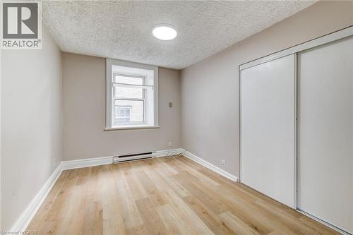 Unfurnished bedroom with light wood-type flooring, baseboard heating, a textured ceiling, and a closet - 1331 King Street E, Cambridge, ON - Indoor Photo Showing Other Room