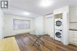 Laundry area with stacked washing machine and dryer, a wall unit AC, dark wood-style floors, and baseboard heating - 