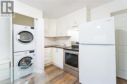 Kitchen with freestanding refrigerator, electric range, white cabinetry, stacked washer and clothes dryer, and dark wood-type flooring - 