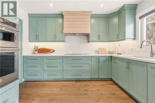 Kitchen featuring green cabinetry, double oven, premium range hood, light wood-style flooring, and decorative backsplash - 697 Lambshead Drive, Burlington, ON - Indoor Photo Showing Kitchen With Upgraded Kitchen