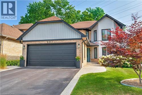 View of front of house featuring a front lawn, asphalt driveway, brick siding, roof with shingles, and an attached garage - 697 Lambshead Drive, Burlington, ON - Outdoor