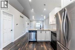 Kitchen with appliances with stainless steel finishes, a peninsula, white cabinetry, dark wood-type flooring, and lofted ceiling - 
