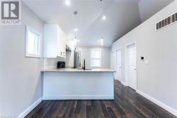 Kitchen with white cabinets, light stone counters, dark wood-style flooring, a peninsula, and vaulted ceiling - 