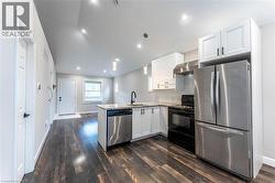 Kitchen with stainless steel appliances, white cabinets, tasteful backsplash, a peninsula, and dark wood finished floors - 