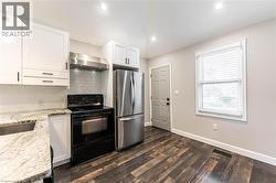Kitchen with electric range, freestanding refrigerator, backsplash, white cabinets, and light stone countertops - 