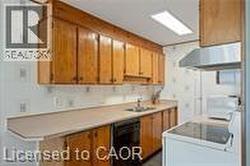 Kitchen with dishwasher, under cabinet range hood, light countertops, brown cabinets, and a sink - 