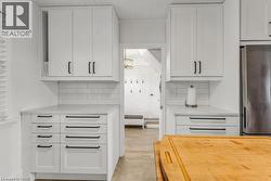 Kitchen with white cabinetry, freestanding refrigerator, light stone counters, and backsplash - 