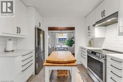 Kitchen with backsplash, stainless steel appliances, white cabinetry, and light stone countertops - 