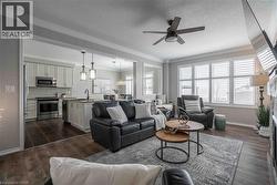 Living room featuring crown molding, dark wood finished floors, a fireplace with raised hearth, ceiling fan and huge windows complete with wood California shutters. - 