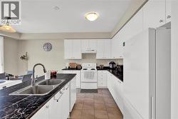 Kitchen featuring white appliances, white cabinetry, dark countertops, and hanging light fixtures - 
