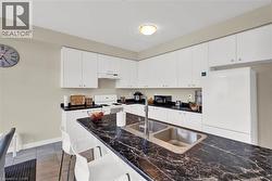 Kitchen with a breakfast bar, white appliances, white cabinets, dark stone counters, and dark tile patterned floors - 
