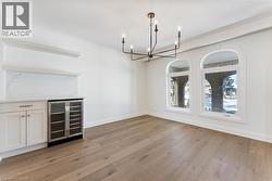 Unfurnished dining area with wine cooler, light wood-style flooring, crown molding, and a chandelier - 