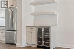 Kitchen featuring high end refrigerator, wine cooler, white cabinetry, light wood-style flooring, and light stone countertops - 