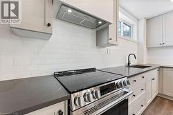 Kitchen featuring stainless steel electric stove, extractor fan, dark stone counters, dark wood-type flooring, and white cabinetry - 