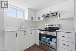 Kitchen featuring stainless steel electric stove, under cabinet range hood, white cabinetry, and light countertops - 