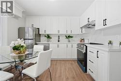 Kitchen with range with electric stovetop, freestanding refrigerator, light wood-style flooring, white cabinetry, and under cabinet range hood - 