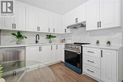 Kitchen with white cabinets, stainless steel appliances, under cabinet range hood, and light wood-type flooring - 