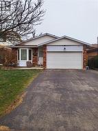 Backsplit home with an attached garage, brick siding, driveway, and a front lawn - 