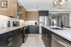 Kitchen with stainless steel appliances, wall chimney range hood, light stone counters, dark cabinets, and arched walkways - 