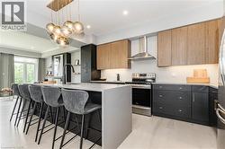 Kitchen featuring modern cabinets, stainless steel appliances, wall chimney exhaust hood, pendant lighting, and an island with sink - 