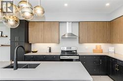 Kitchen with stainless steel range with electric cooktop, wall chimney range hood, modern cabinets, dark cabinetry, and recessed lighting - 