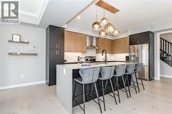 Kitchen with appliances with stainless steel finishes, decorative light fixtures, modern cabinets, a breakfast bar area, and wall chimney exhaust hood - 