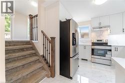 Kitchen with stainless steel appliances, white cabinets, light marble finish flooring, and under cabinet range hood - 