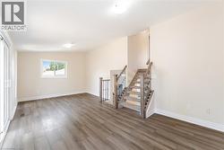 Unfurnished living room featuring wood finished floors, stairway, and lofted ceiling - 