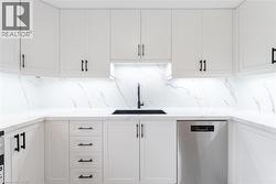 Kitchen with light stone countertops, stainless steel dishwasher, white cabinets, and backsplash - 