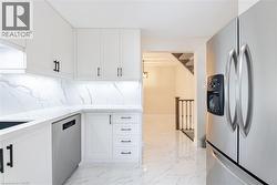 Kitchen with stainless steel appliances, light stone counters, light marble finish floors, and white cabinetry - 
