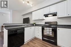 Kitchen with black appliances, white cabinetry, under cabinet range hood, and dark countertops - 
