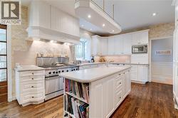 Kitchen with wallpapered walls, white cabinets, a kitchen island with sink, stainless steel appliances, and dark wood-style flooring - 